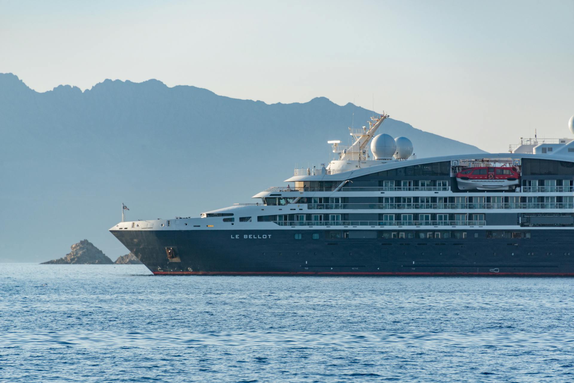 A sleek black cruise ship sails past majestic mountains on a clear day.