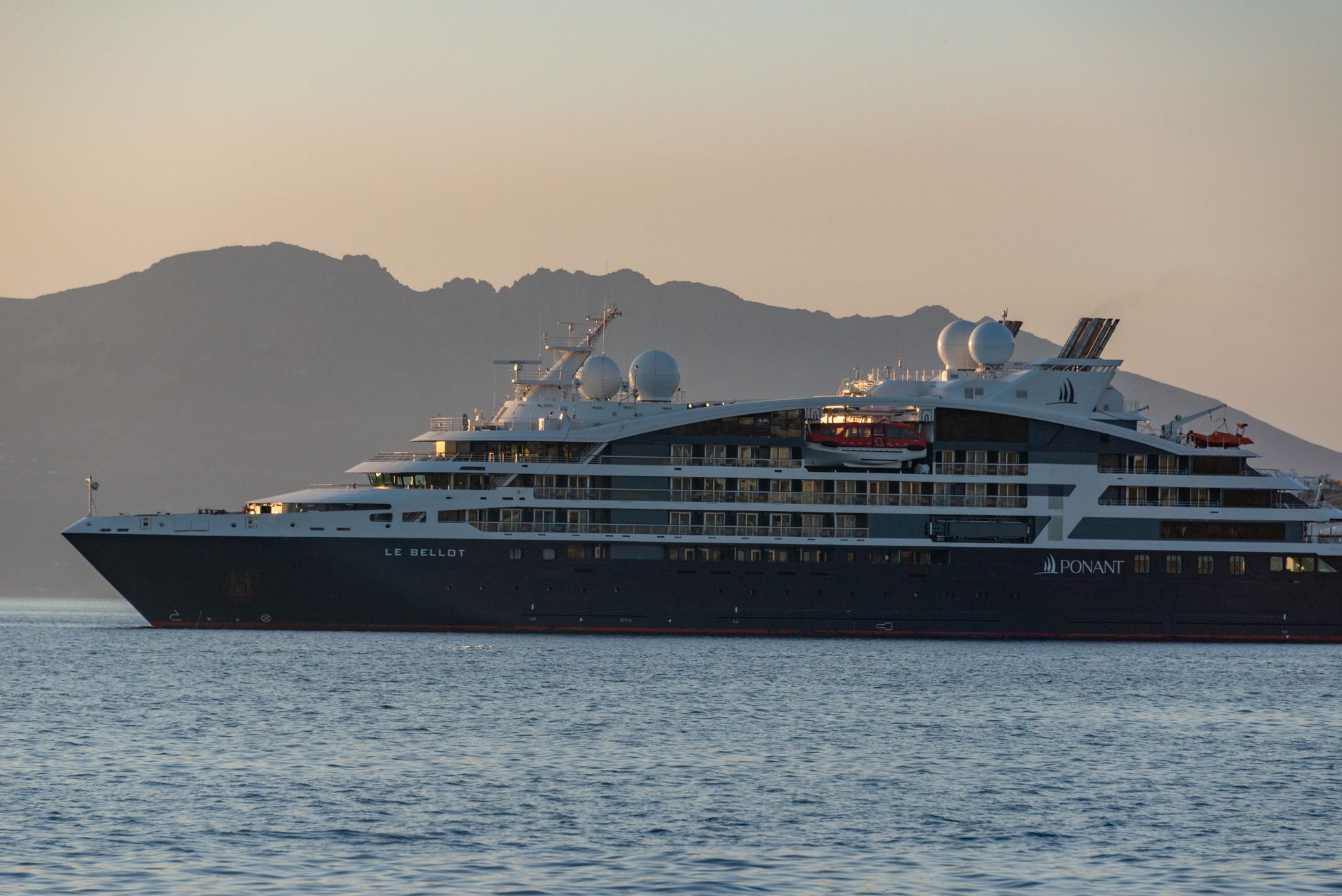 A stunning cruise ship sailing at sunset with a mountainous backdrop.