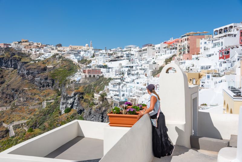 A woman stands on a balcony overlooking the iconic white houses of Santorini, Greece.
