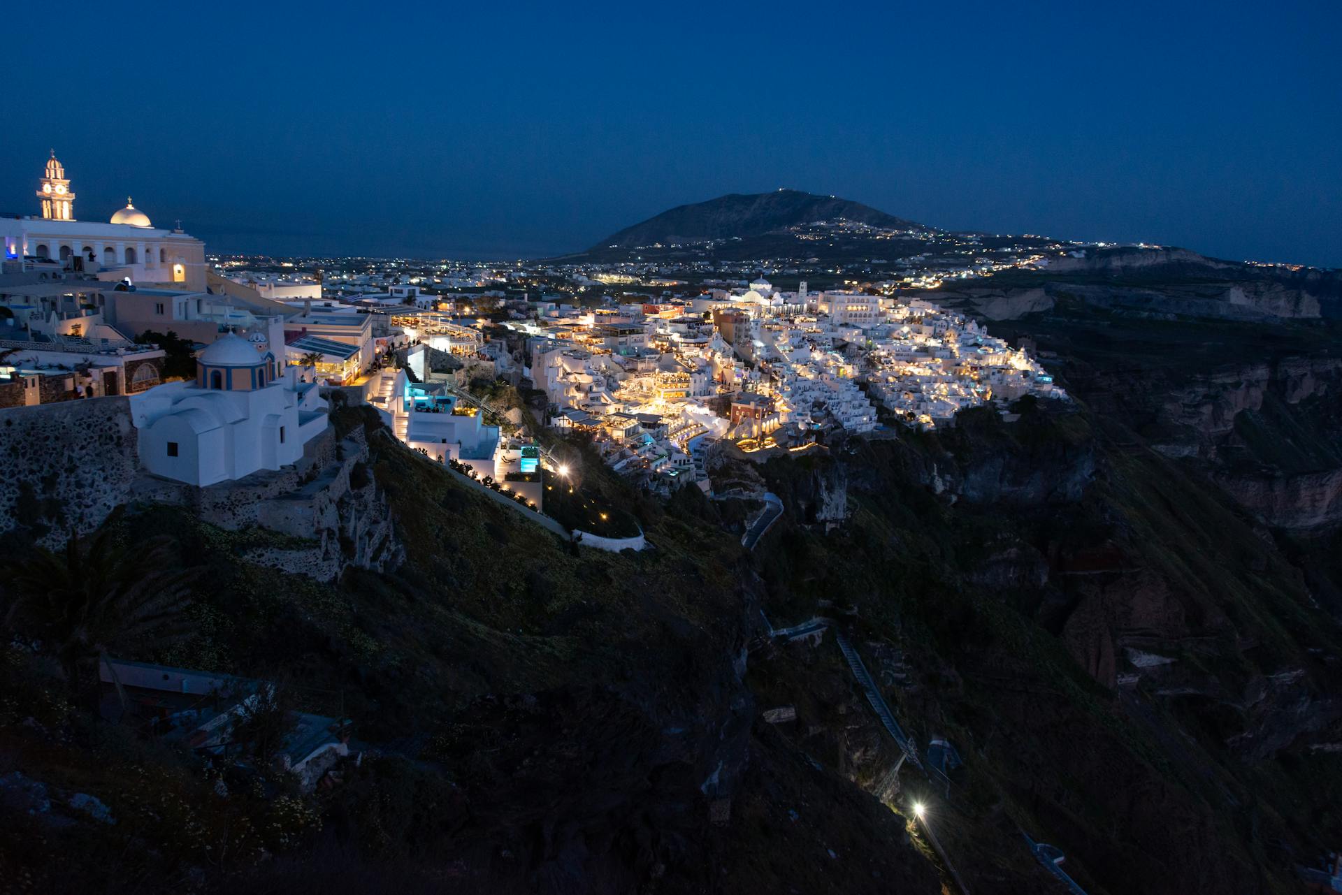 Stunning night view of illuminated Santorini town against a sapphire blue sky.