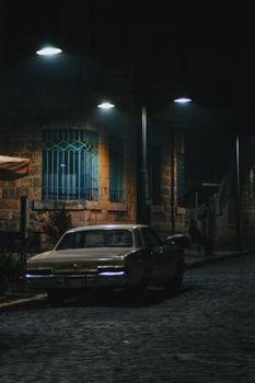 A classic vintage car parked under street lights on a cobblestone road in Tarsus, Türkiye.