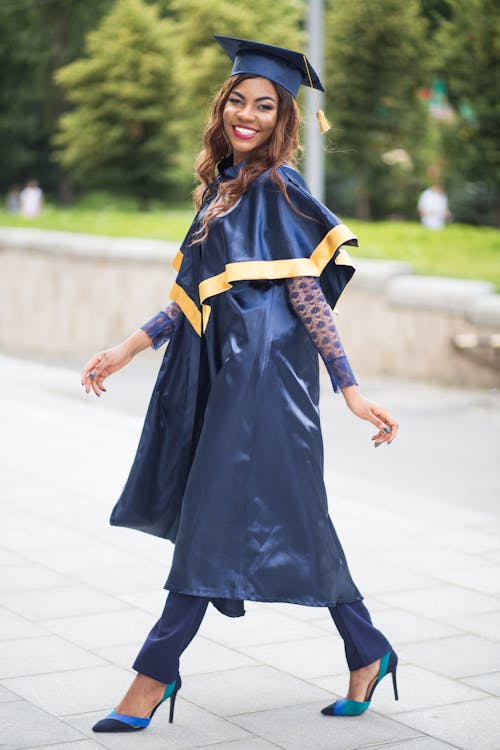 Photo of a Smiling Woman Wearing a Navy Blue Graduation Gown and High Heels