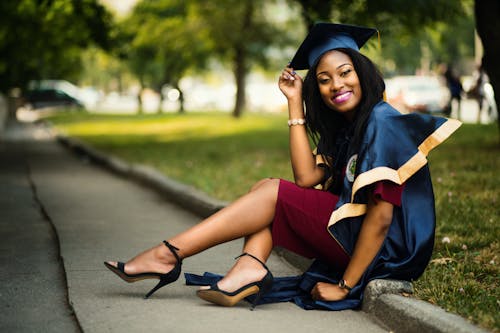 Female Graduate Student Wearing a Mortarboard Sitting on a Curb in a Park 