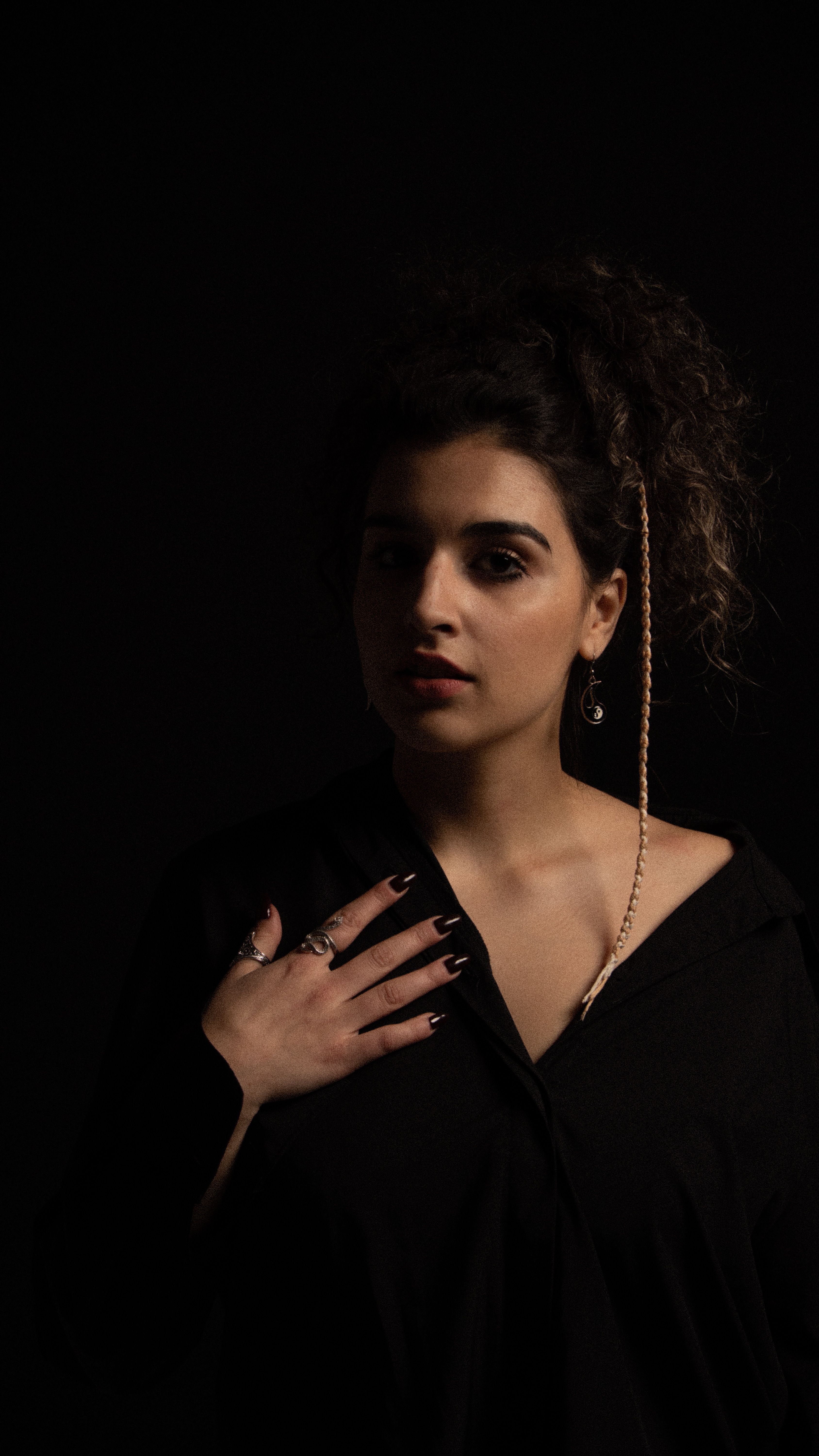 Portrait of a sophisticated woman in dark attire against black backdrop, exuding elegance.