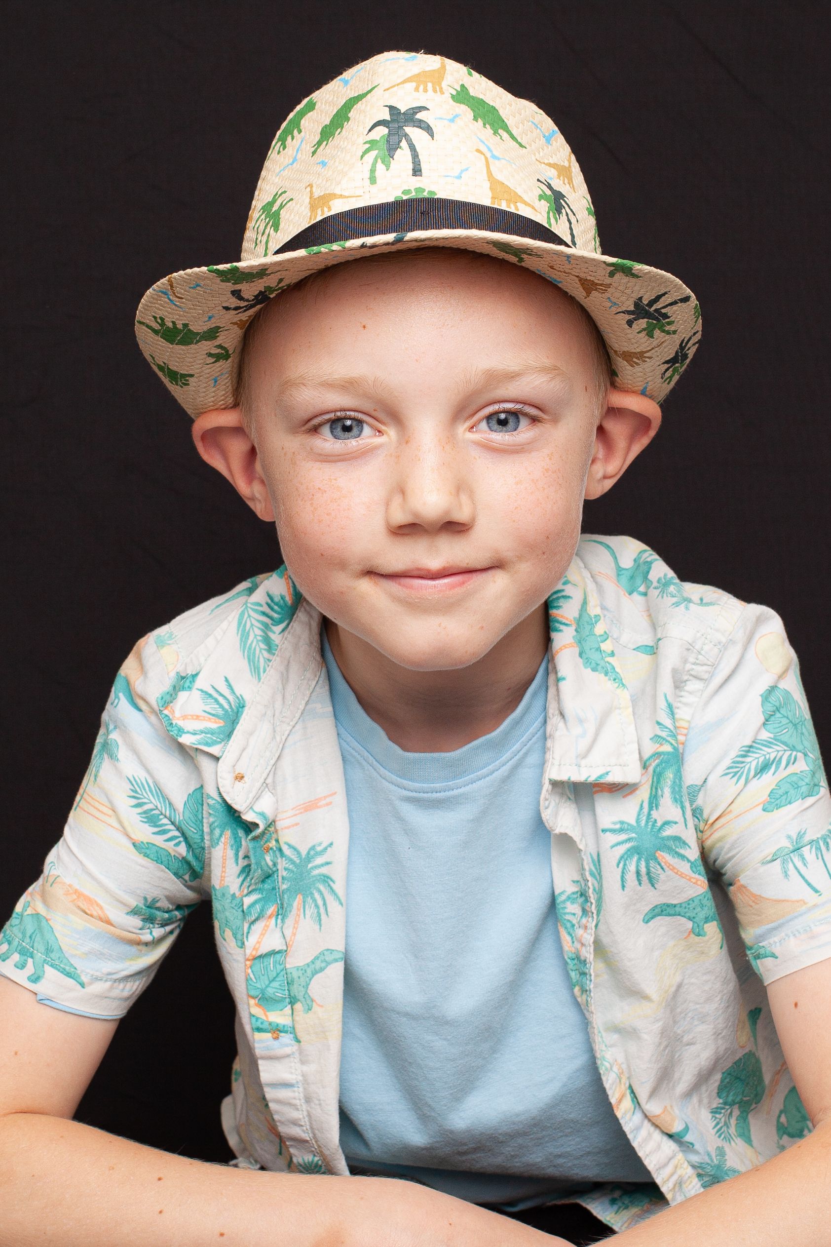 Portrait of a smiling boy in a tropical hat and shirt against a black background.