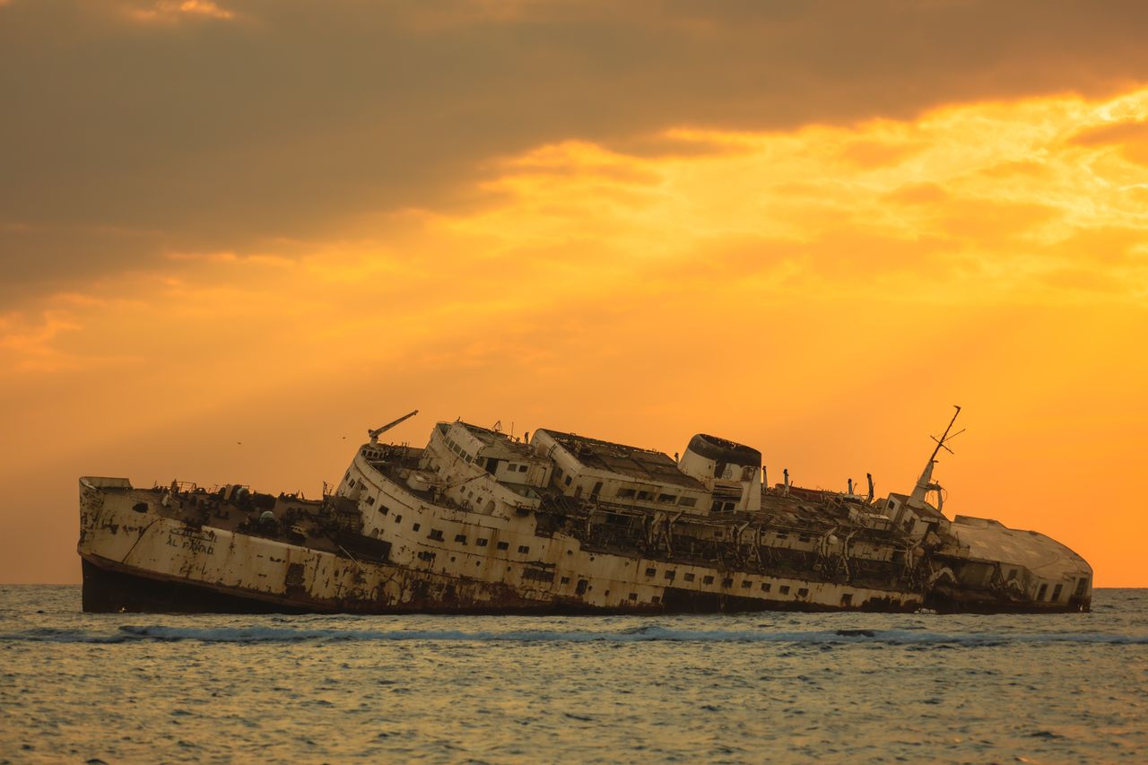 photograph of a decaying shipwreck against a golden sunset in the wate