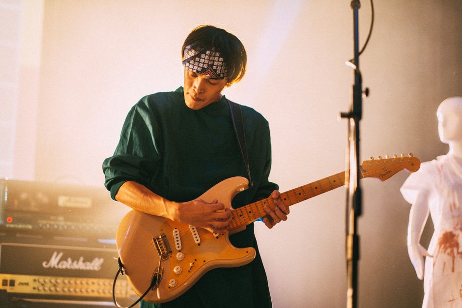 Musician in concert playing electric guitar with mannequin on stage.