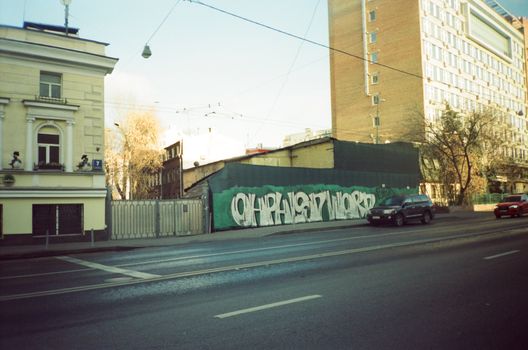 Street view in Moscow featuring graffiti on a wall and passing cars.
