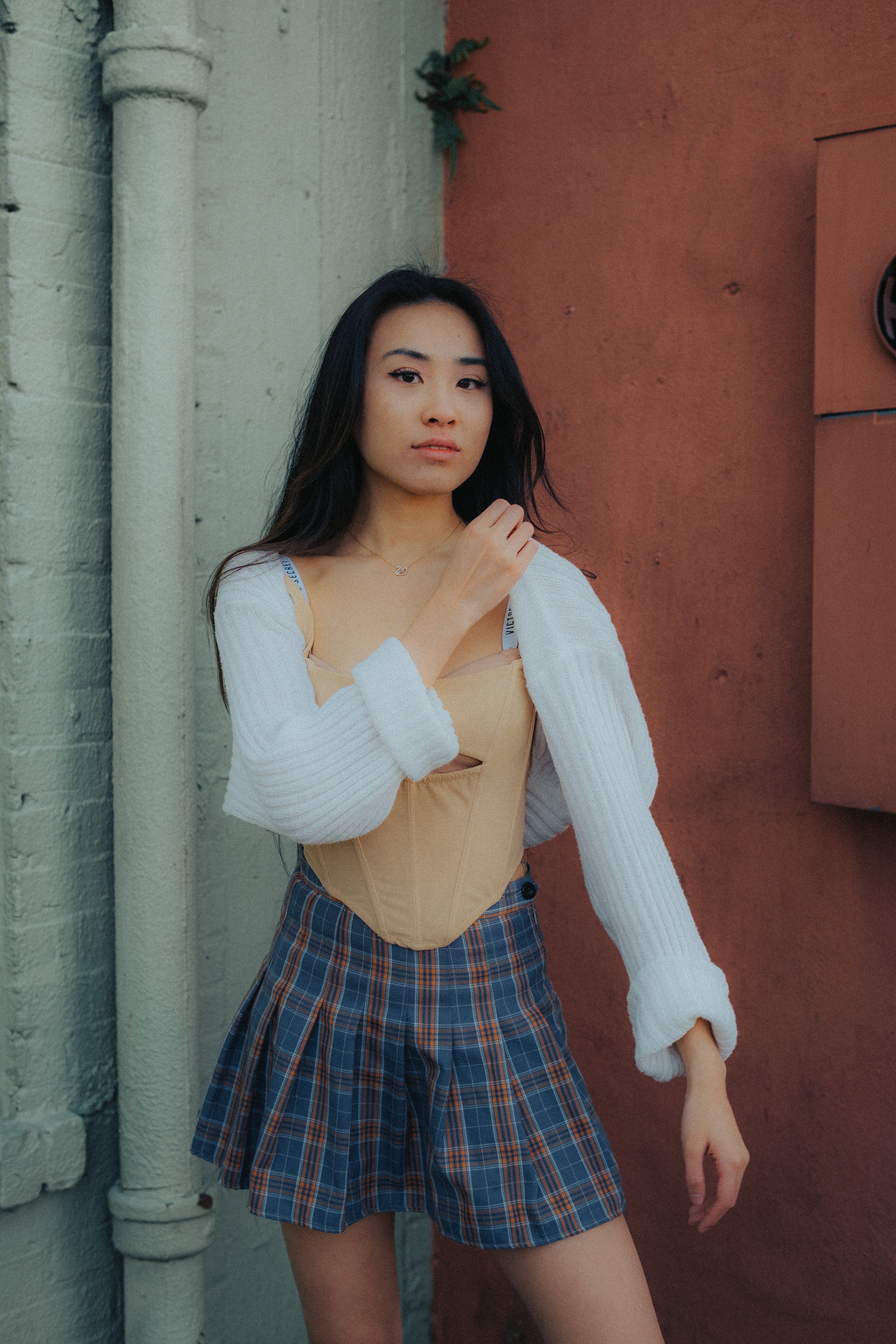 Asian woman in fashionable outfit posing against urban walls, showcasing elegance and style.