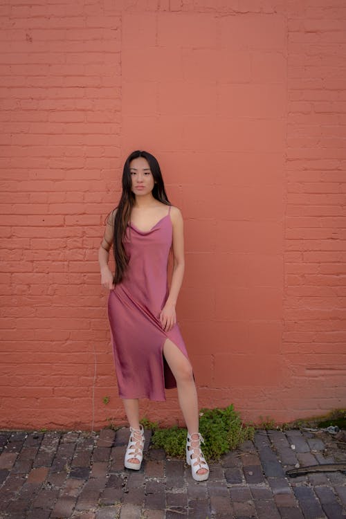Woman in Pink Spaghetti Strap Dress Standing beside Brick Wall