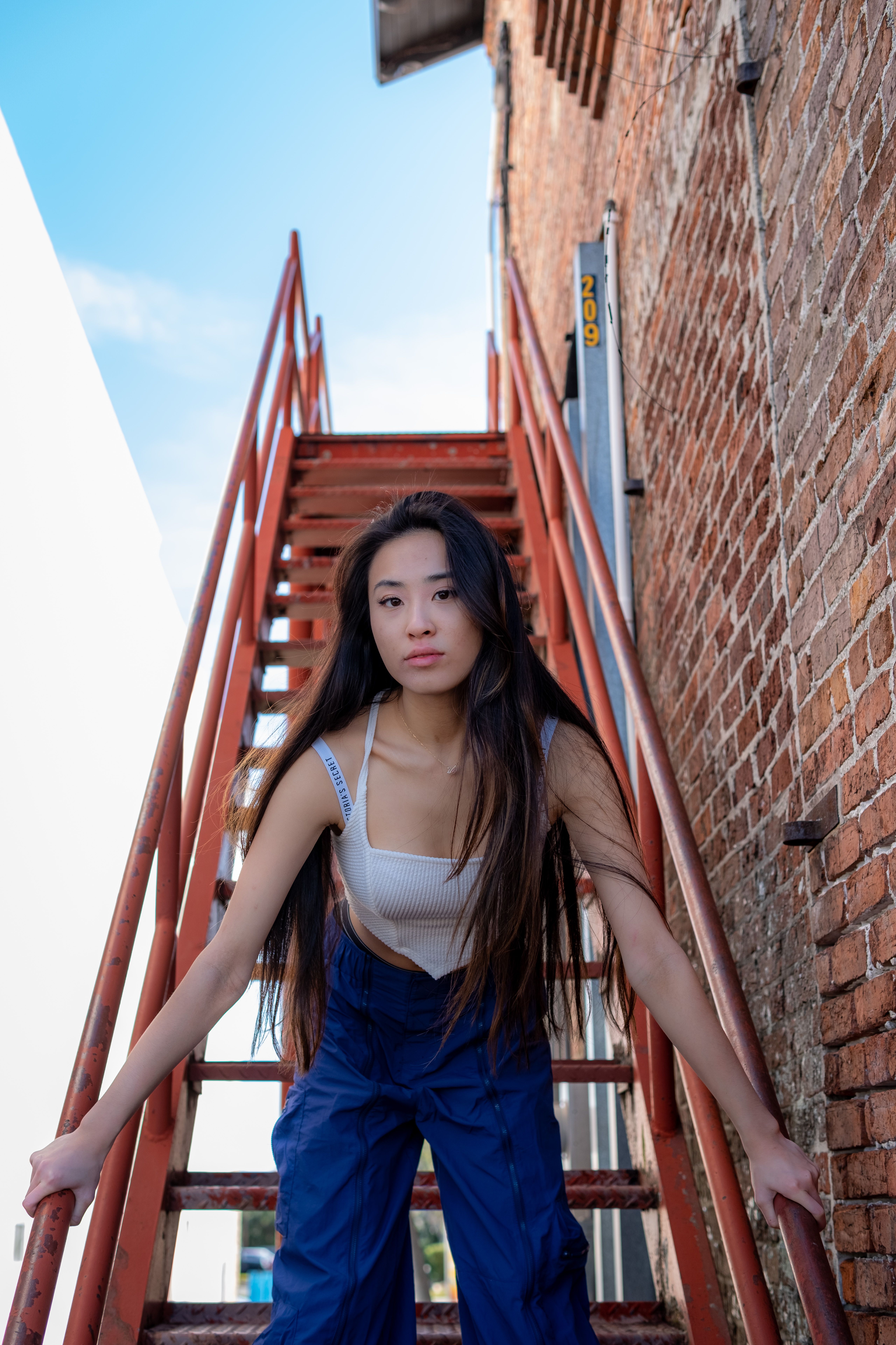 Portrait of a young woman leaning on a staircase against a brick wall outside.