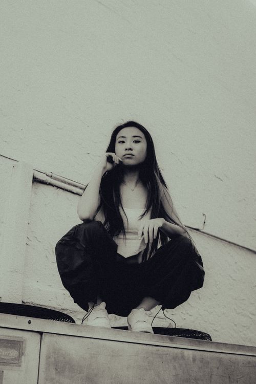 Free Black and white photo of a stylish woman in streetwear, crouching outdoors. Stock Photo