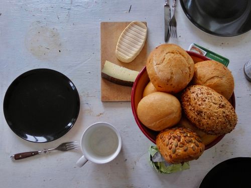 Free A cozy breakfast setting with assorted rolls and cheese on a wooden board. Stock Photo