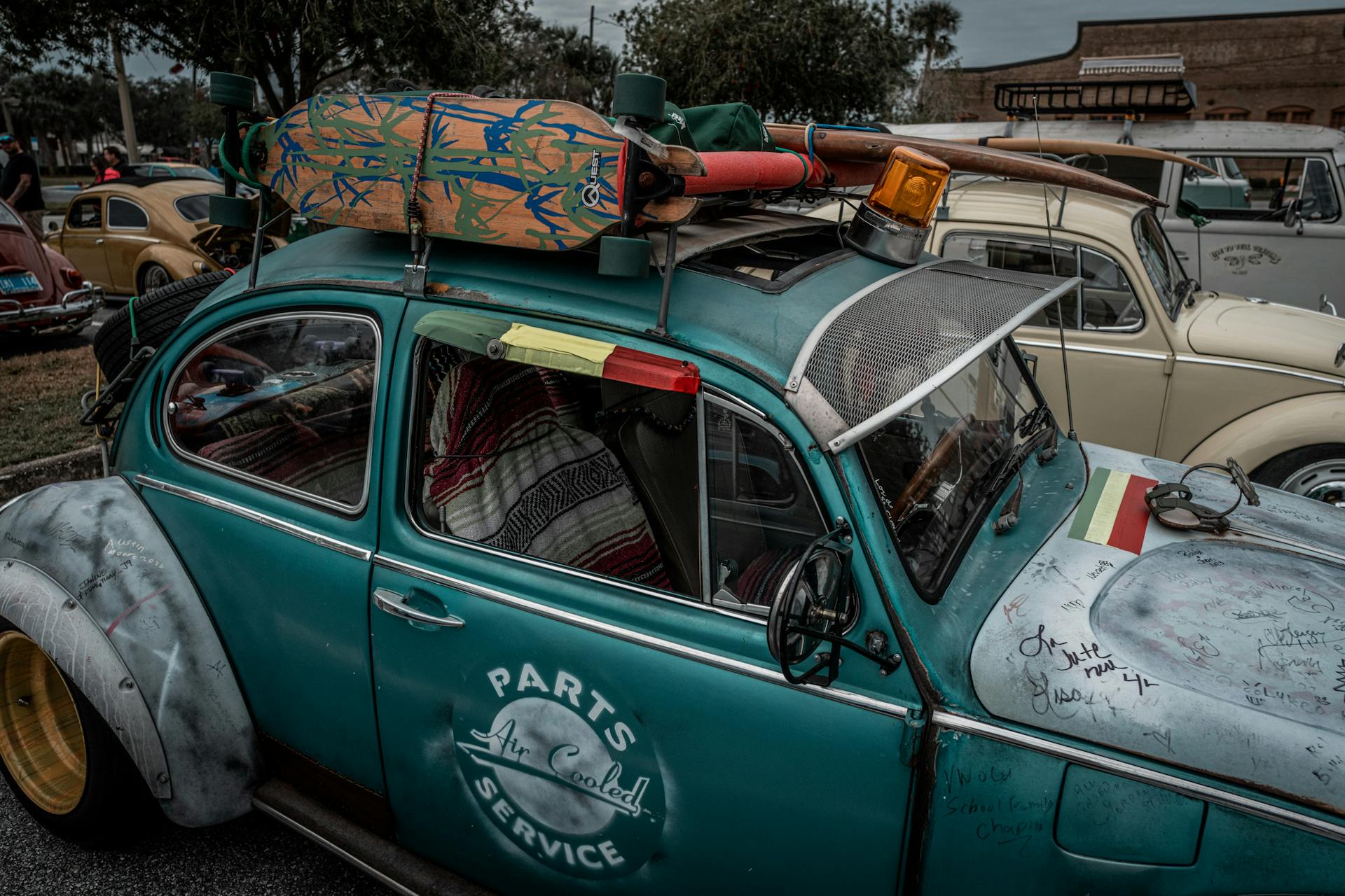 Classic VW Beetle with surfboard and visual mods on display outdoors.