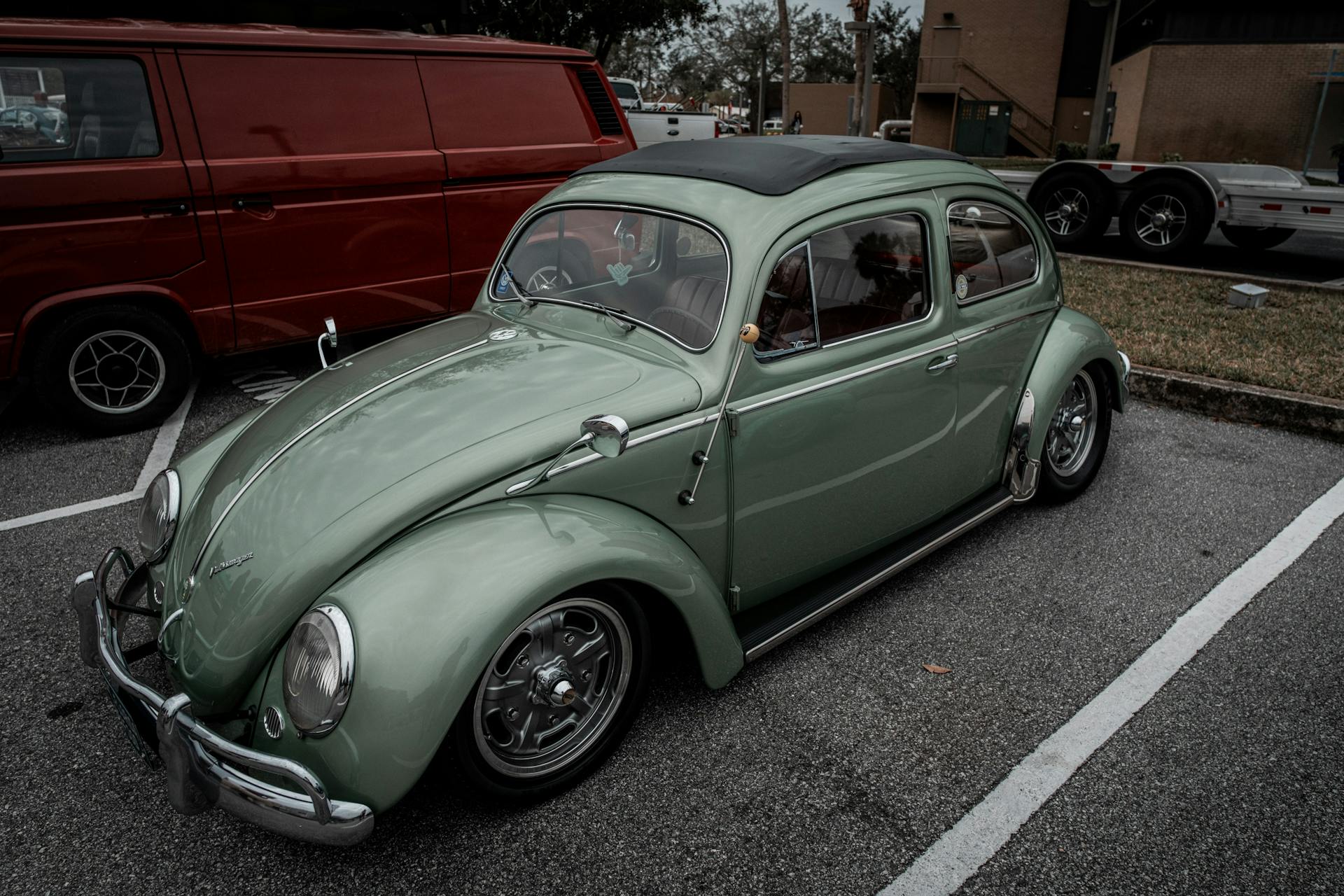 Vintage green Volkswagen Beetle with sunroof in a parking lot, evoking nostalgia.