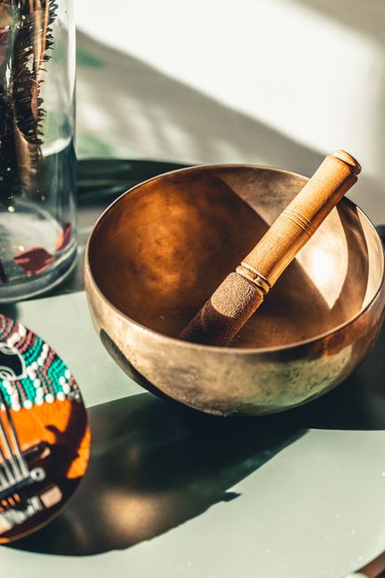 A copper singing bowl and mallet create serene vibes on a sunlit table.