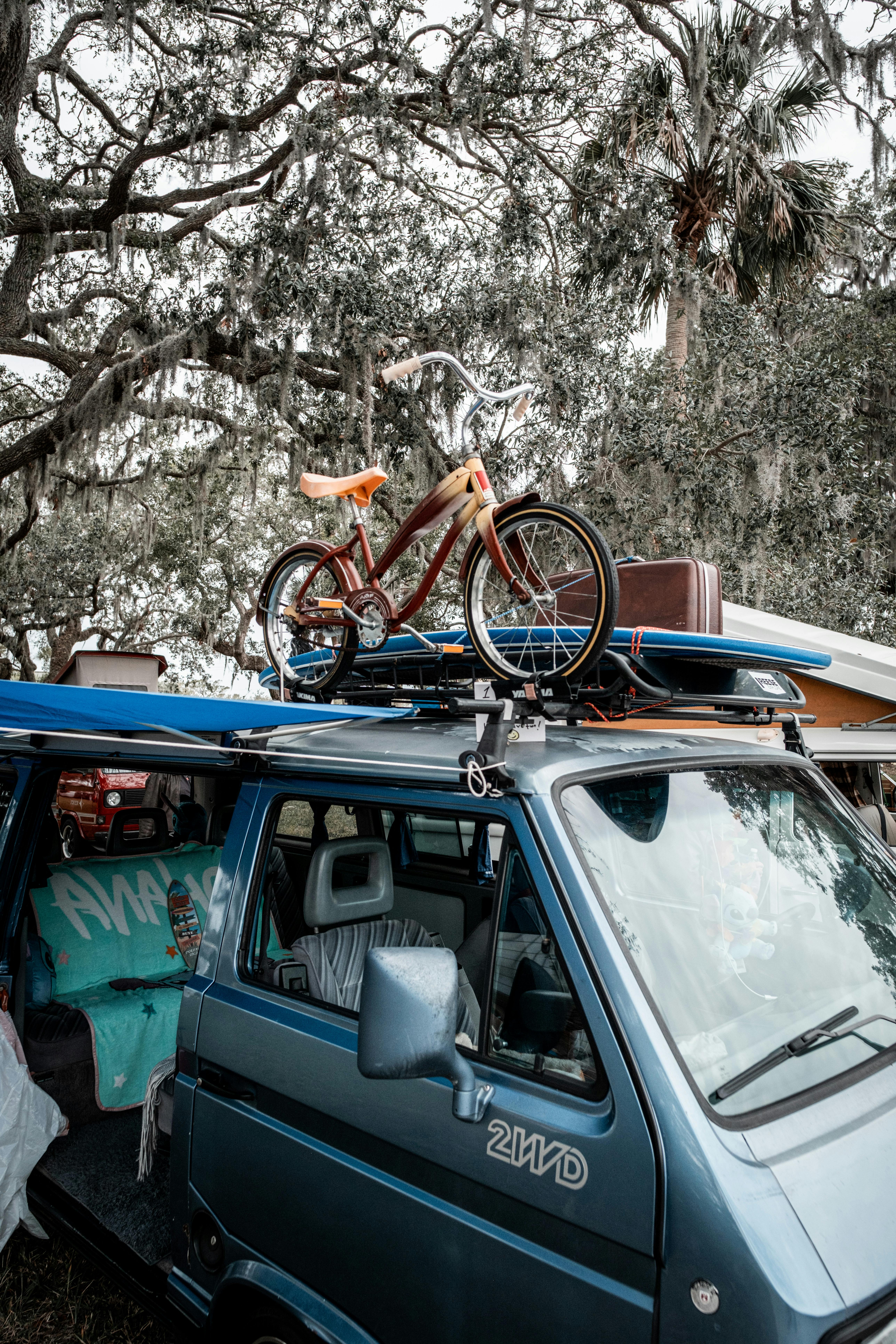 Vintage van with bicycle and surfboard under shady trees, adventure-ready.