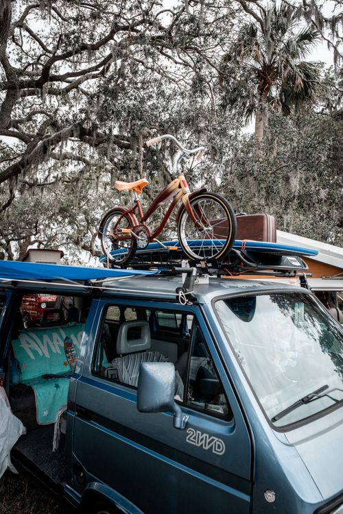 Free Vintage van with bicycle and surfboard under shady trees, adventure-ready. Stock Photo