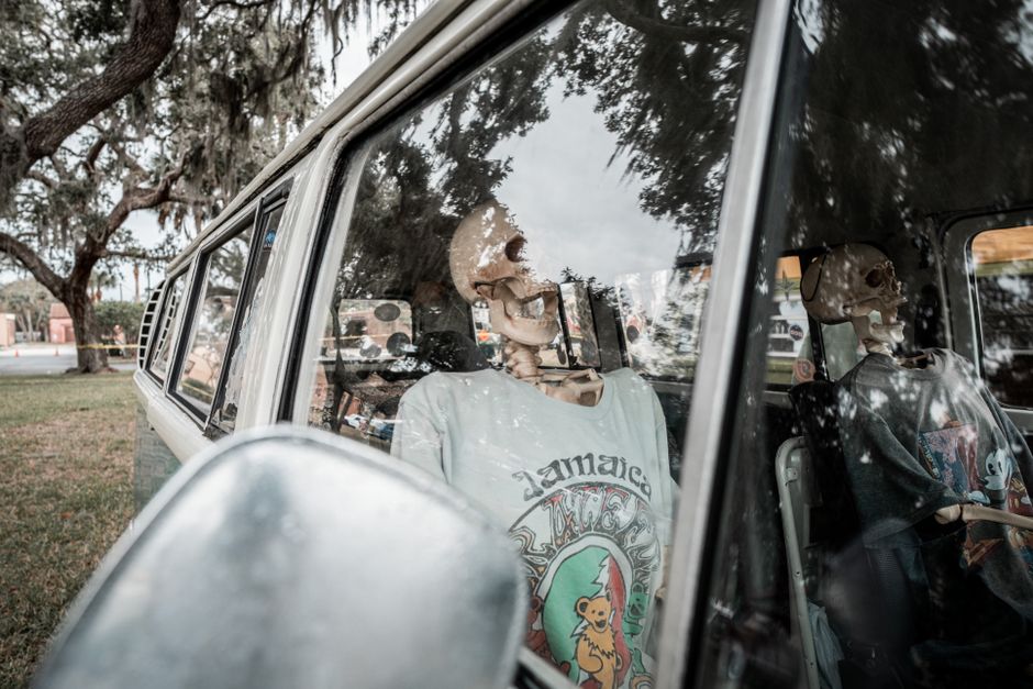 Skeletons dressed in shirts occupy a vintage van, creating a humorous scene.
