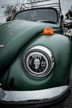 Detailed view of a vintage Volkswagen Beetle headlight and green exterior, showcasing retro design.