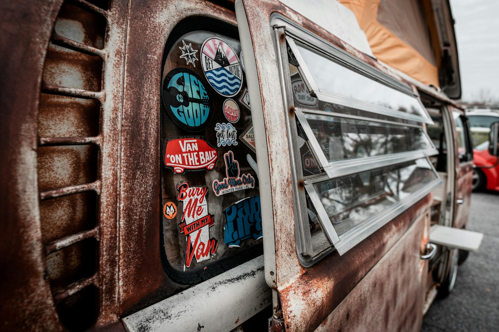 Close-up of a rusty vintage Volkswagen camper van with colorful stickers and rooftop tent.