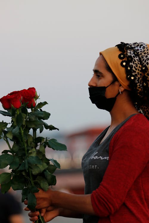 Woman in Face Mask Carrying Red Roses