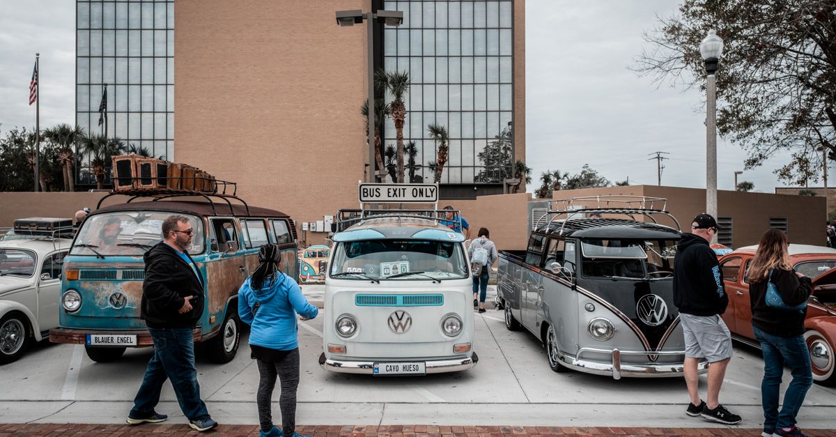 Retro Volkswagen vans and cars gathered for a car meet in city parking space.