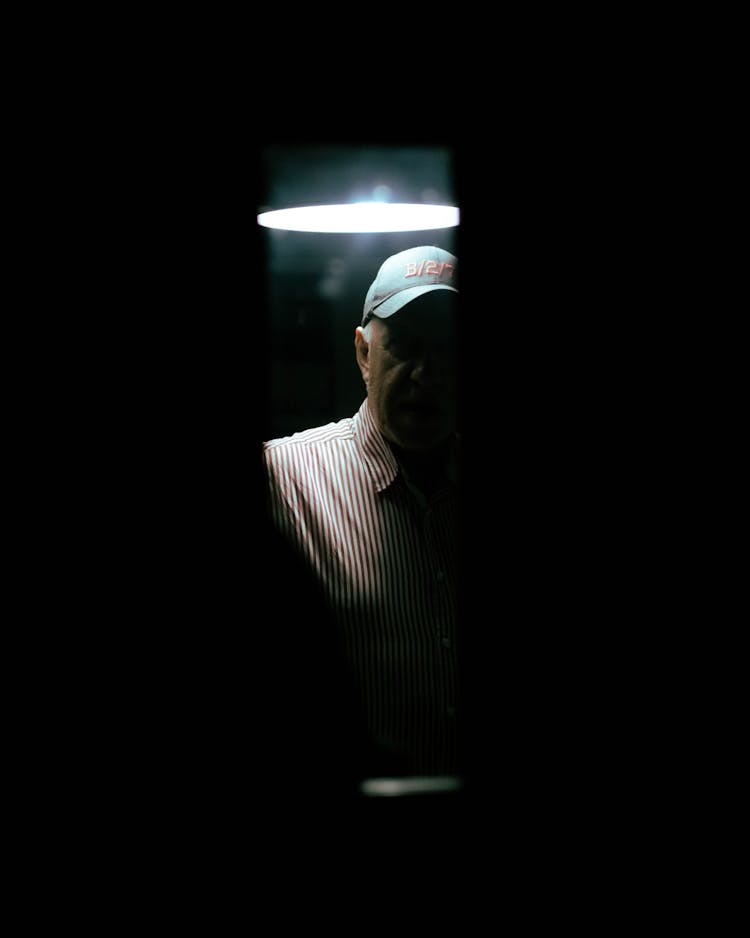 Man In Hat Under Lamp In Dark