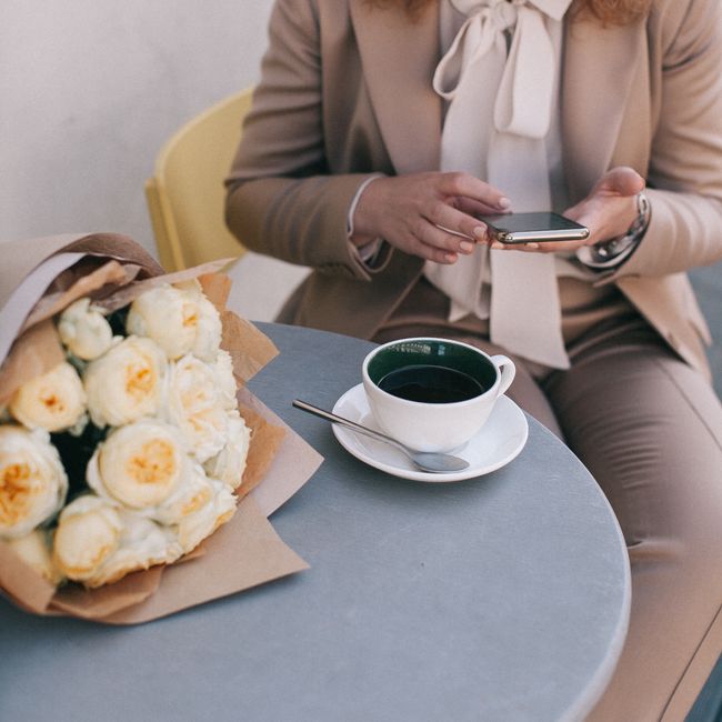 A woman enjoying coffee with a bouquet at a stylish café table.