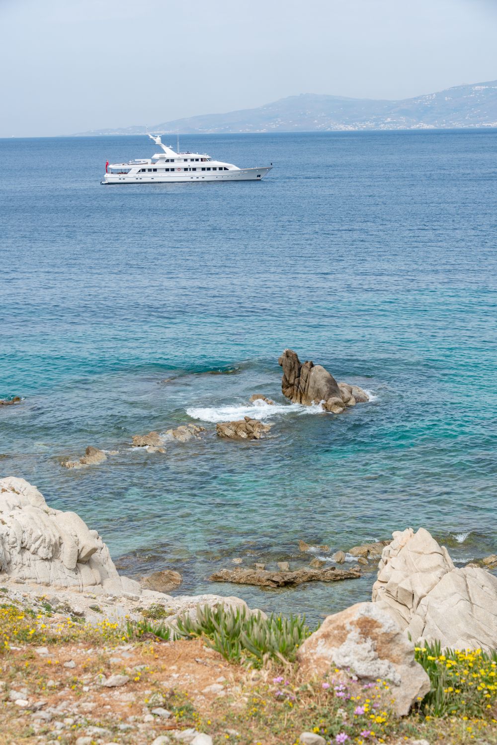 Yacht anchored off a rocky shoreline in clear water