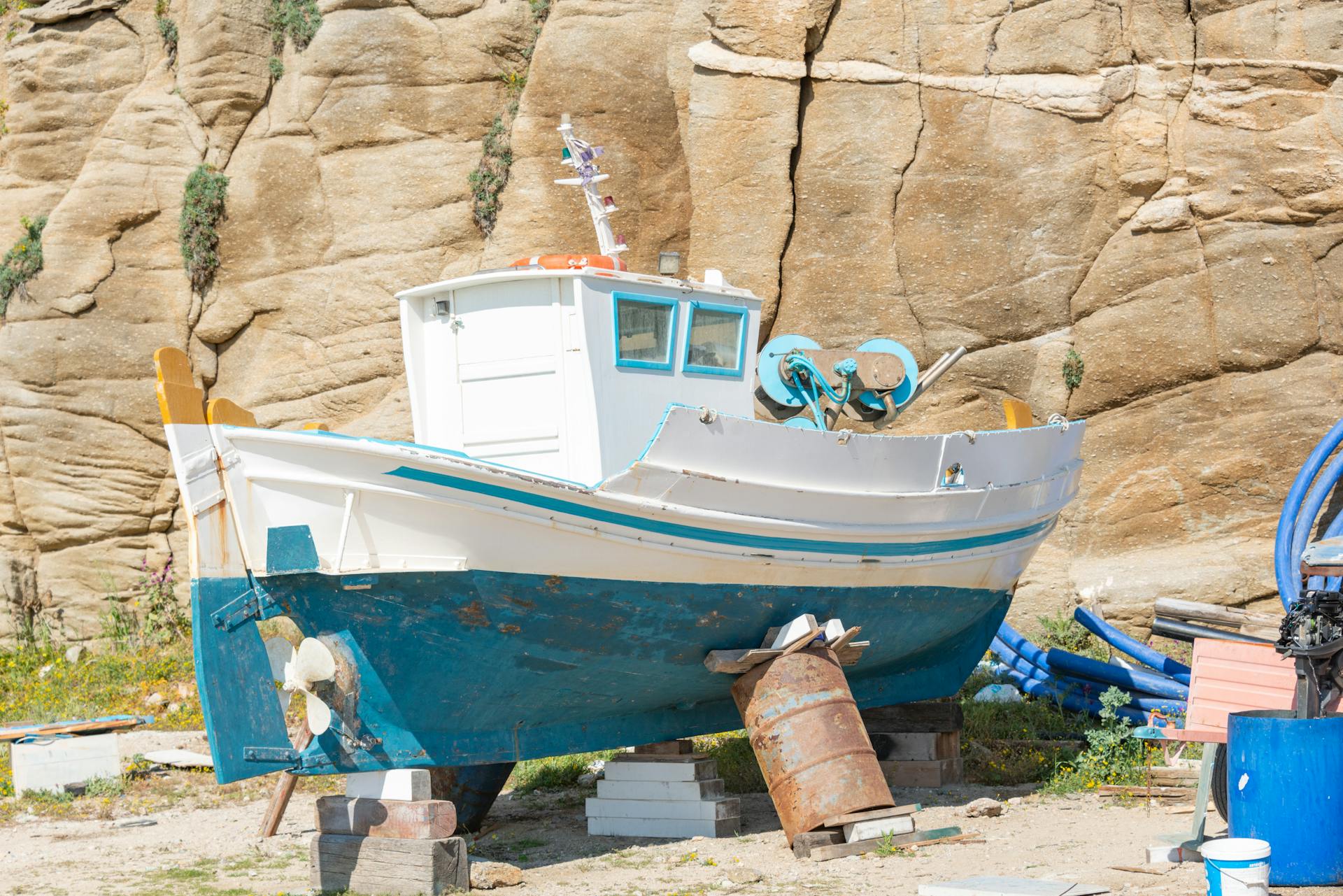 A traditional fishing boat rests on a dry dock against a rocky cliff, capturing a serene coastal scene.
