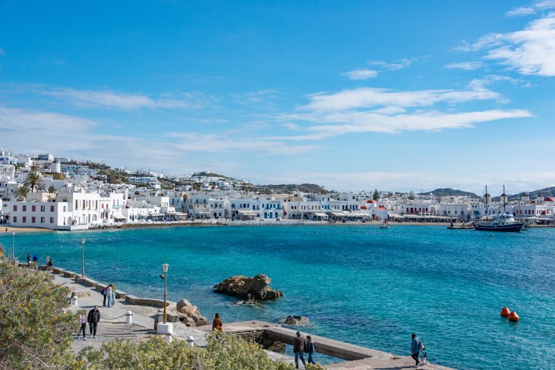 Beautiful view of Mykonos town with people strolling by the blue Aegean Sea.