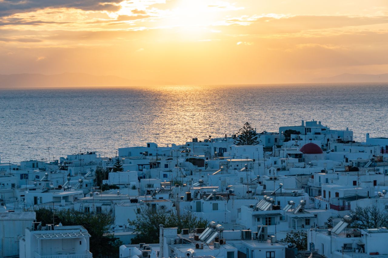 The terrace at Krama set for dinner in the evening light, with Mykonos Town and the sea beyond.