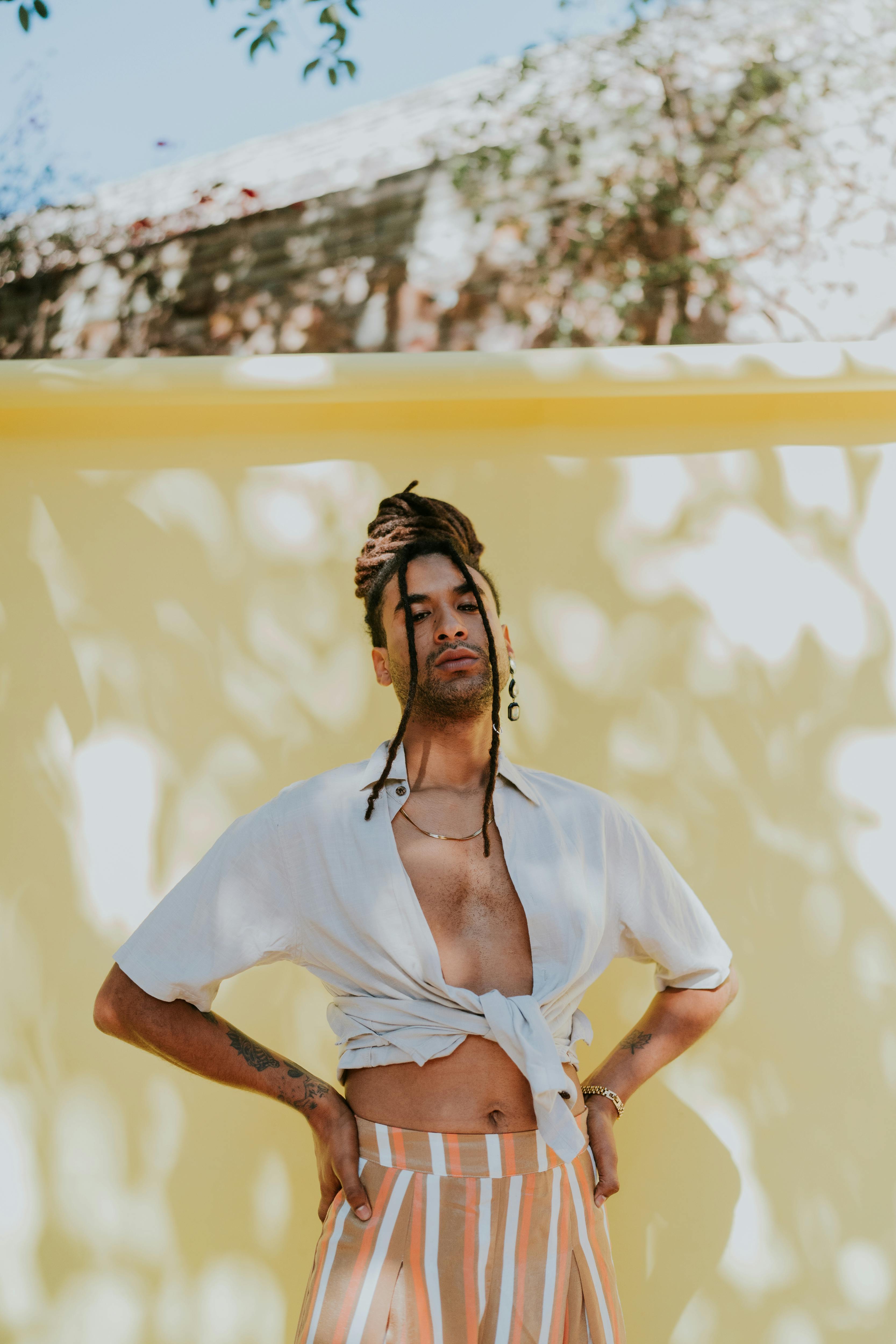 Fashionable young man posing confidently against a vibrant yellow backdrop. Sunlit, modern style.