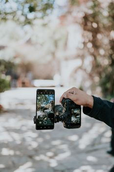 Person capturing photos with DSLR camera and smartphone in outdoor setting.
