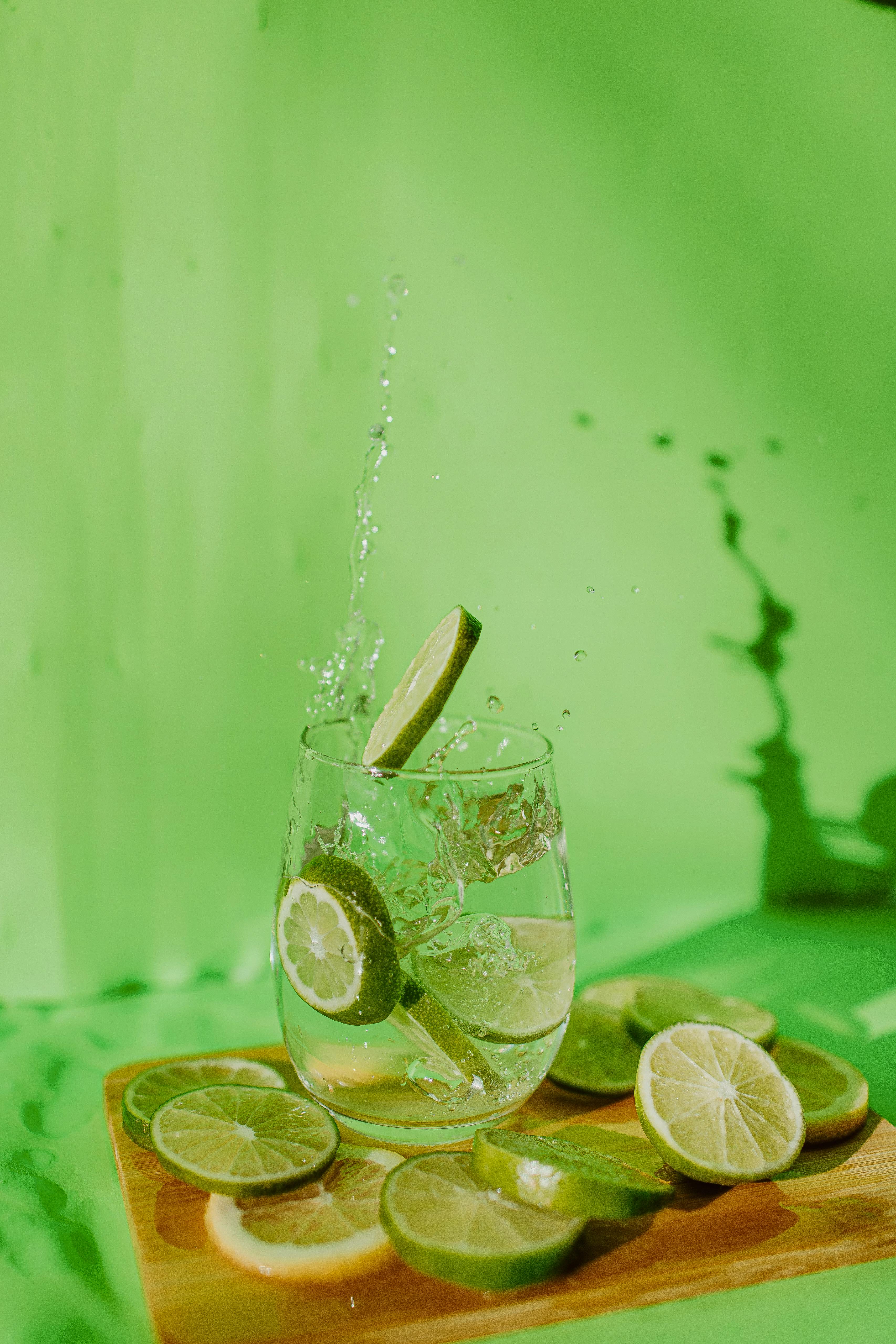 Lime slices splashing into water against vibrant green background.