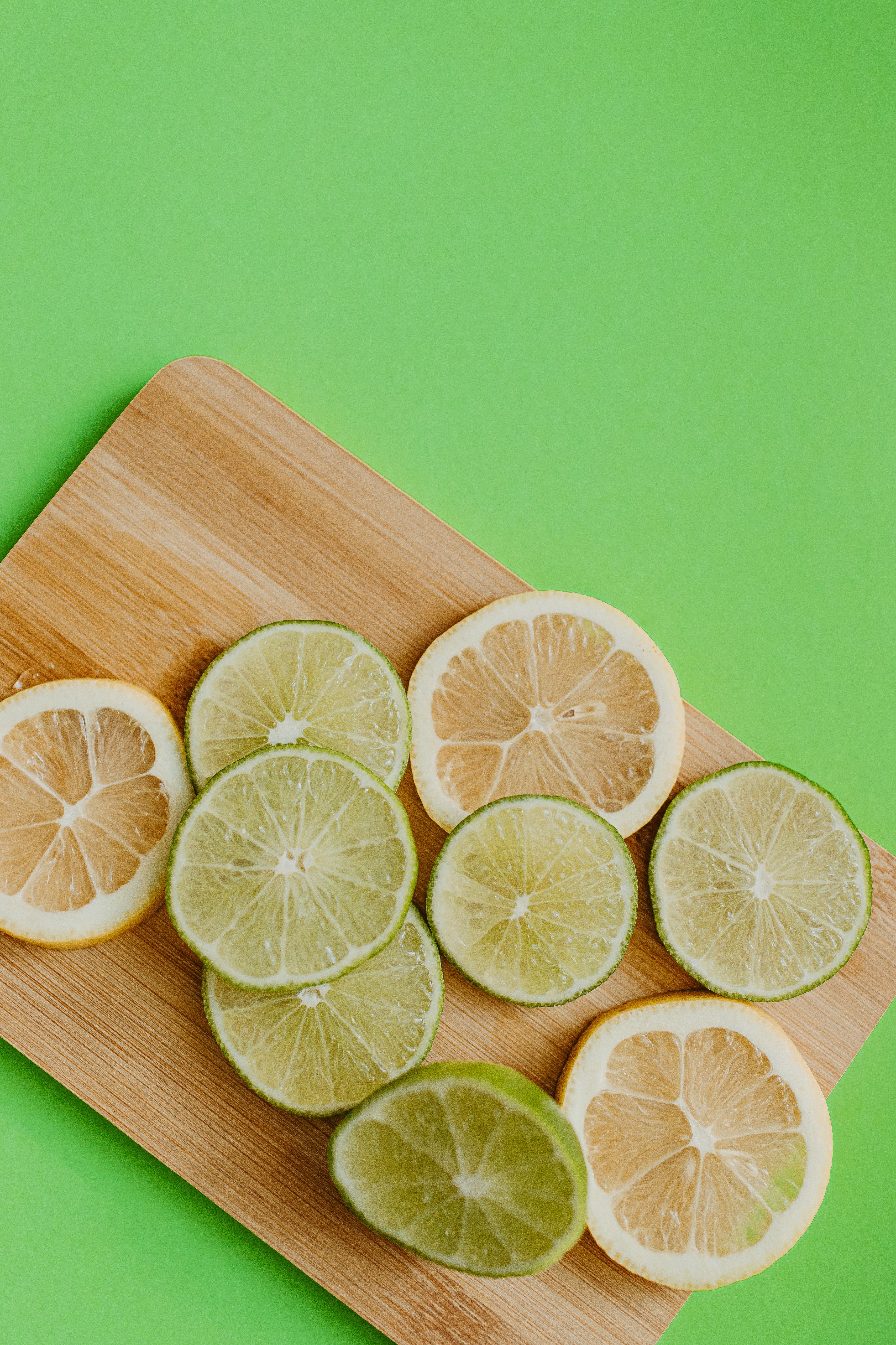 A vibrant display of lemon and lime slices on a bamboo board against a green background.