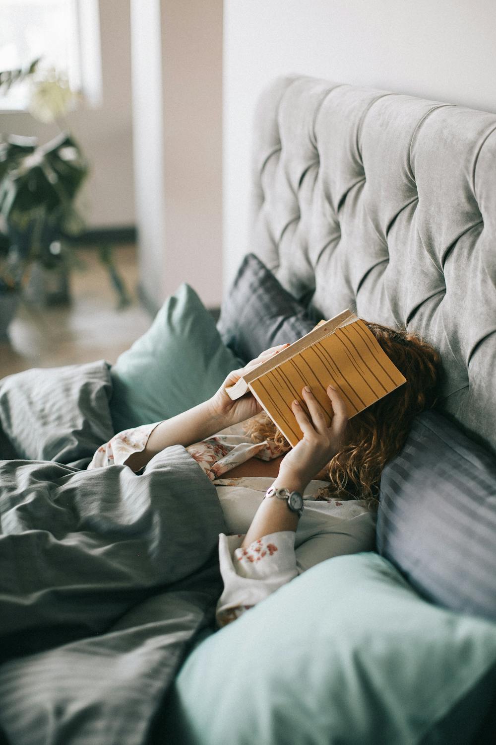woman in bed with book covering her face