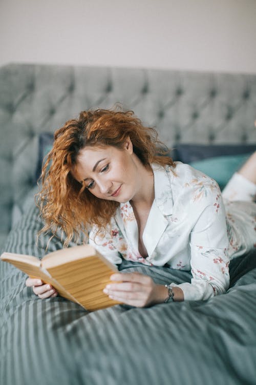 Woman Laying On Bed While Reading Book