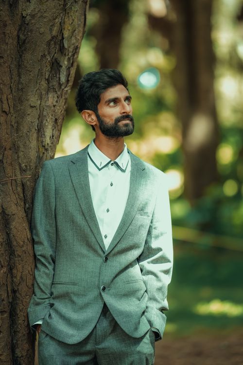 Free A man in a grey suit stands by a tree in a park, looking thoughtfully at his surroundings. Stock Photo