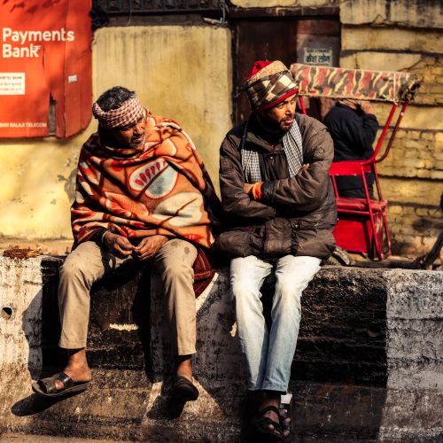 Free Two men in warm clothing sitting on a street bench, conveying urban life. Stock Photo