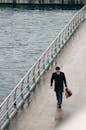 一个穿着深色西装的商人独自走在水上的现代城市桥梁上