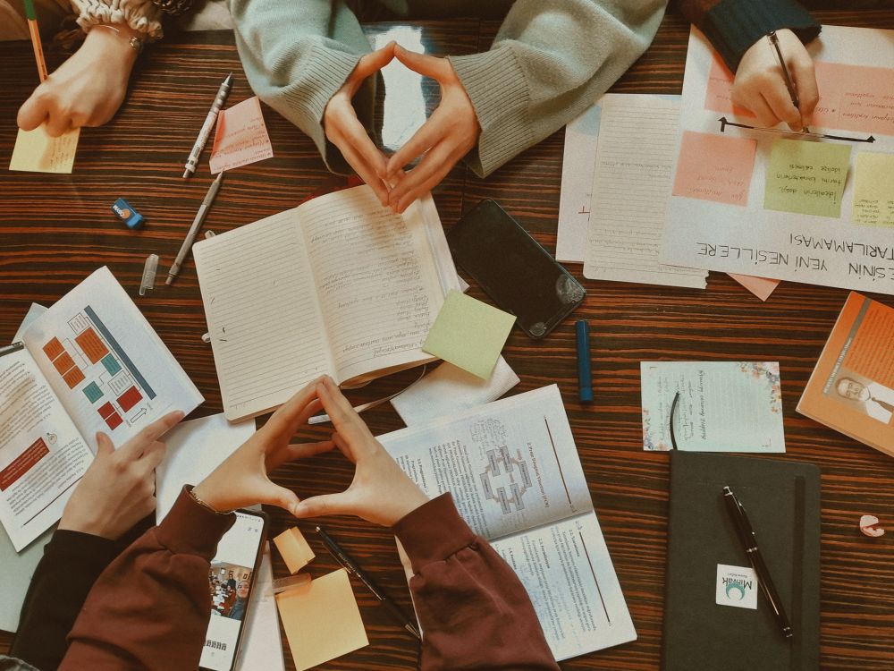 Learners' hands, notebooks and pens around a shared study table