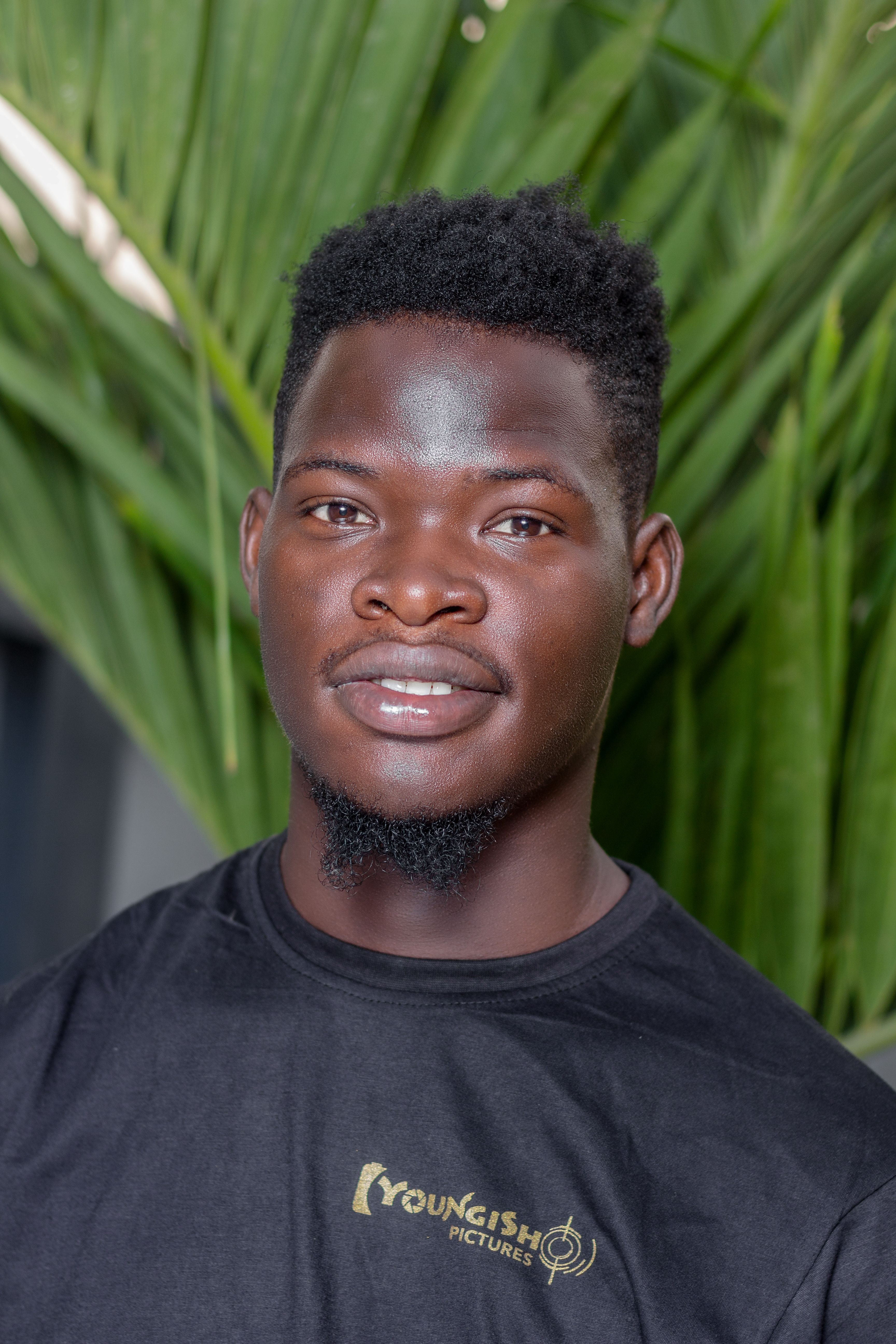 Portrait of a young man smiling in a casual black T-shirt against a green outdoor background.