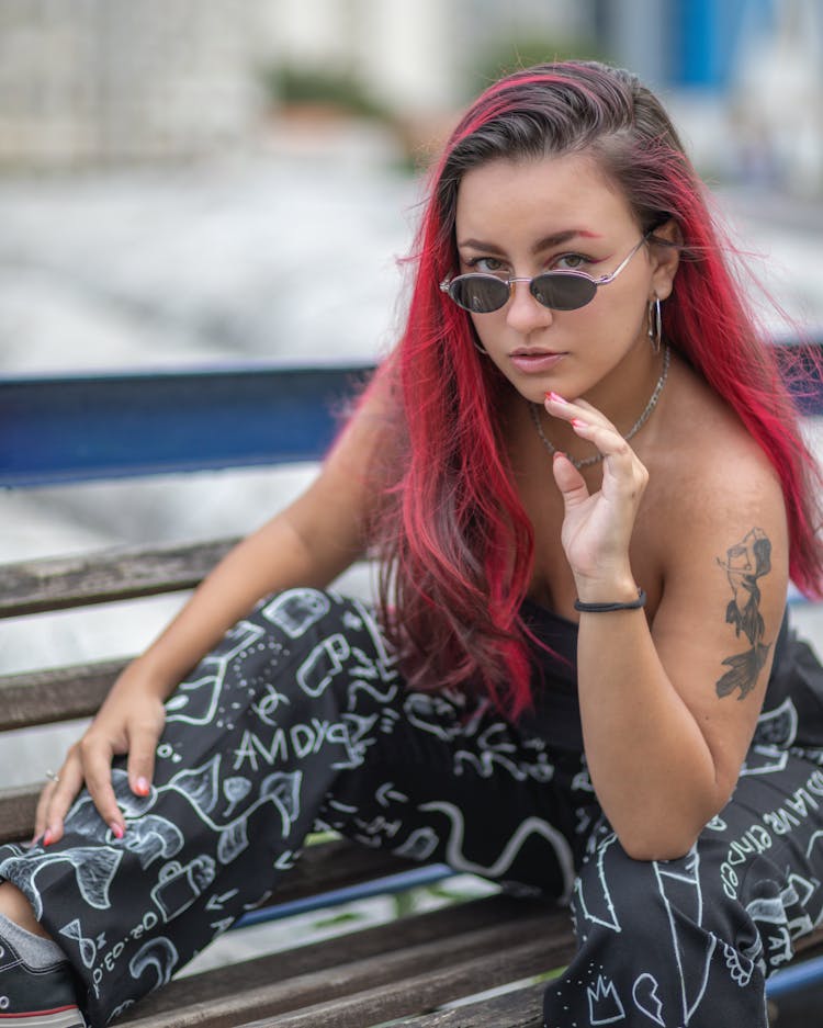 Young Woman With Dyed Hair And Sunglasses Sitting On A Bench 