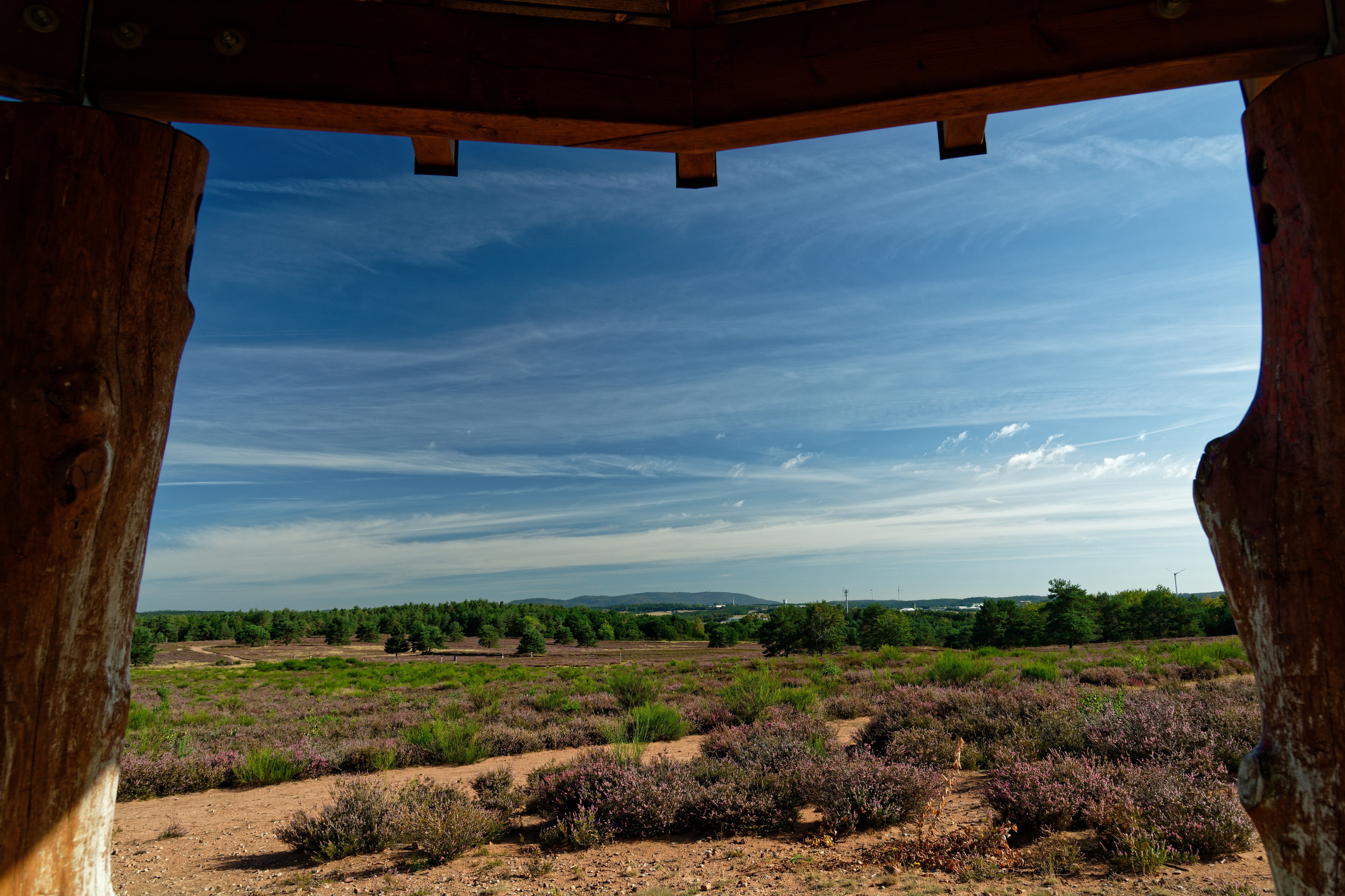 Scenic landscape view framed by wooden posts, showcasing clear blue skies and lush greenery.