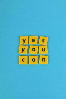 Yellow tiles on blue background spelling 'yes you can', promoting motivation and positivity.