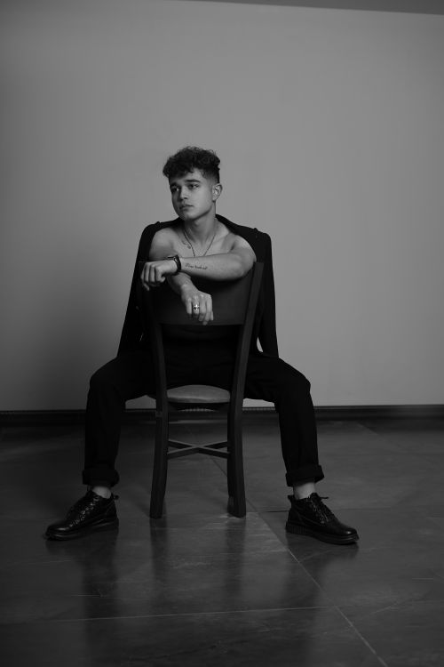 Free Artistic black and white photo of a man sitting on a chair, showcasing modern fashion style and demeanor. Stock Photo