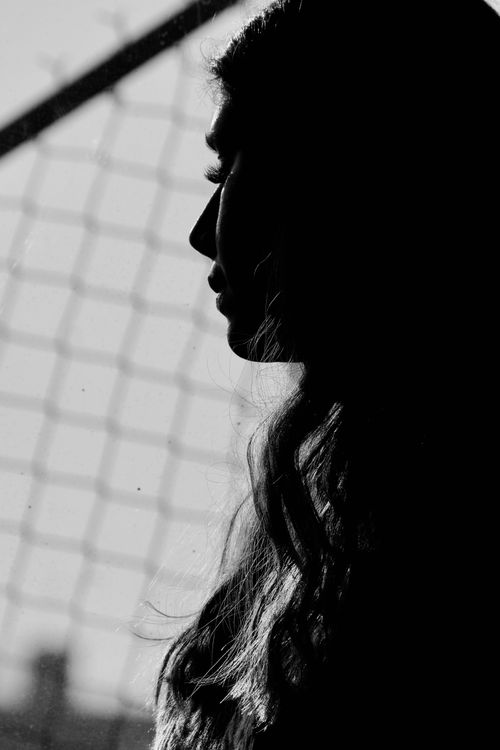 Free Artistic black and white silhouette of a young woman in profile against a wire fence. Stock Photo