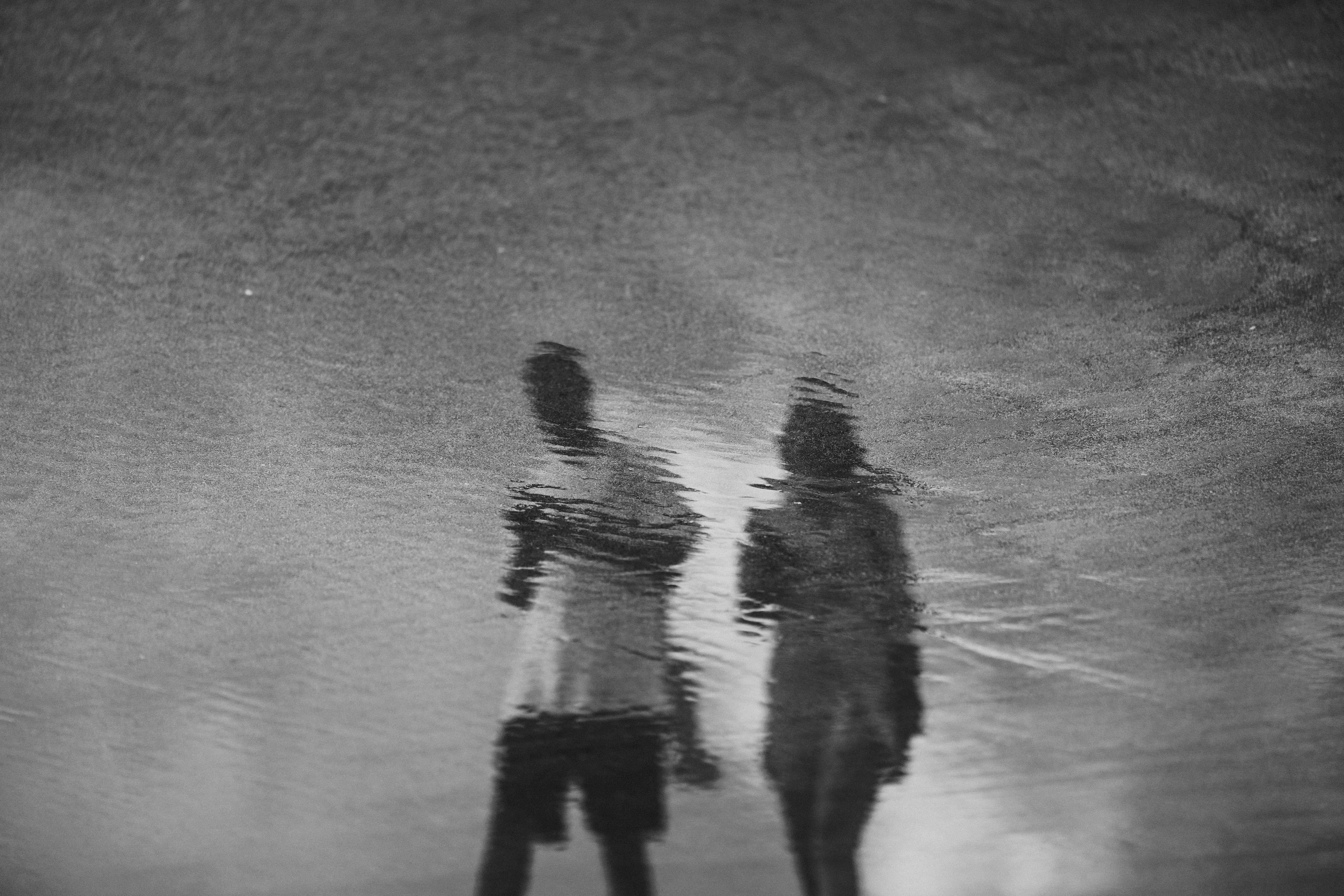 Abstract reflection of a man and woman in a puddle on Kuta Beach, Bali.